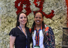 Ginna and Mercy together in front of their wall of pastel flowers and roses.